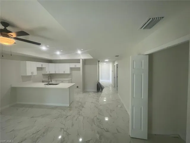 Kitchen featuring kitchen peninsula, ceiling fan, sink, and white cabinets