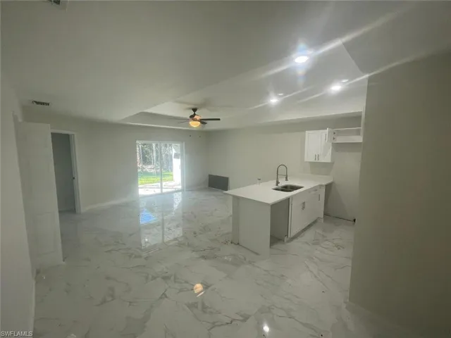 Kitchen with ceiling fan, sink, white cabinetry, and kitchen peninsula