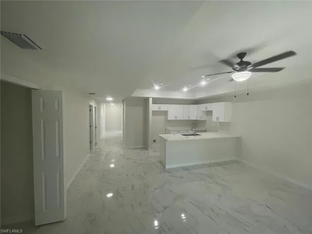 Kitchen featuring kitchen peninsula, white cabinetry, ceiling fan, and sink