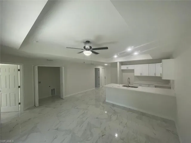 Kitchen featuring ceiling fan, sink, and white cabinets