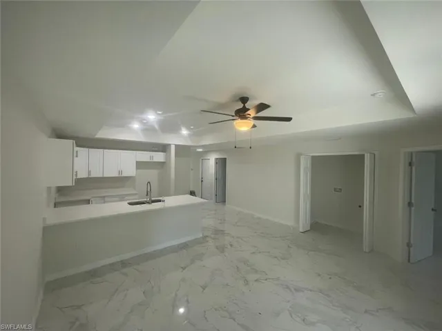 Kitchen featuring white cabinets, a raised ceiling, sink, ceiling fan, and kitchen peninsula