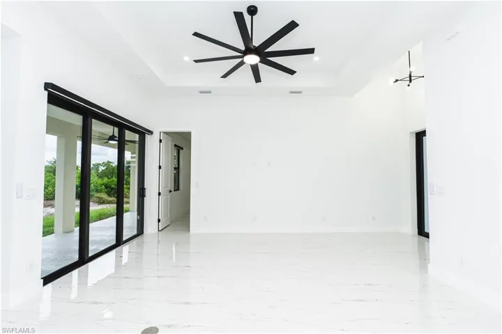 Empty room with ceiling fan, a tray ceiling, light marble finish floors, a towering ceiling, and a chandelier