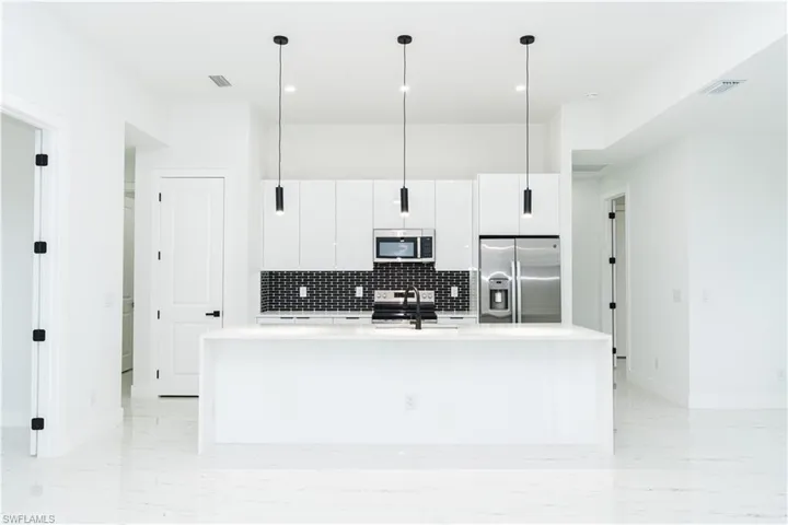 Kitchen with appliances with stainless steel finishes, tasteful backsplash, a kitchen island with sink, light stone counters, and decorative light fixtures