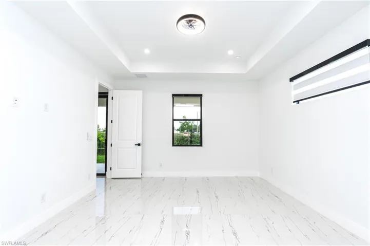 Unfurnished room with a tray ceiling, light marble finish floors, and recessed lighting