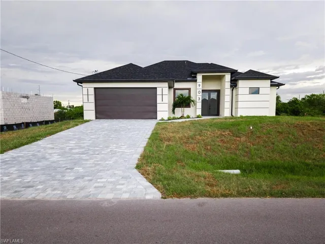 Prairie-style home with decorative driveway, a front yard, stucco siding, and an attached garage