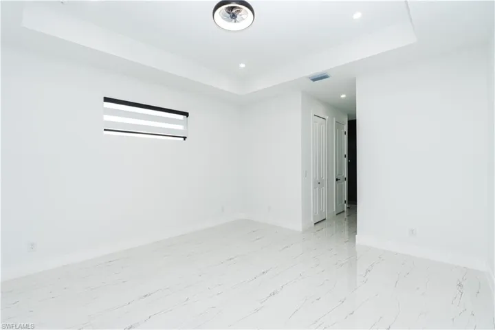Empty room featuring a tray ceiling, recessed lighting, and light marble finish floors