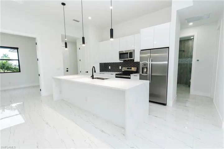 Kitchen featuring backsplash, appliances with stainless steel finishes, pendant lighting, an island with sink, and white cabinets