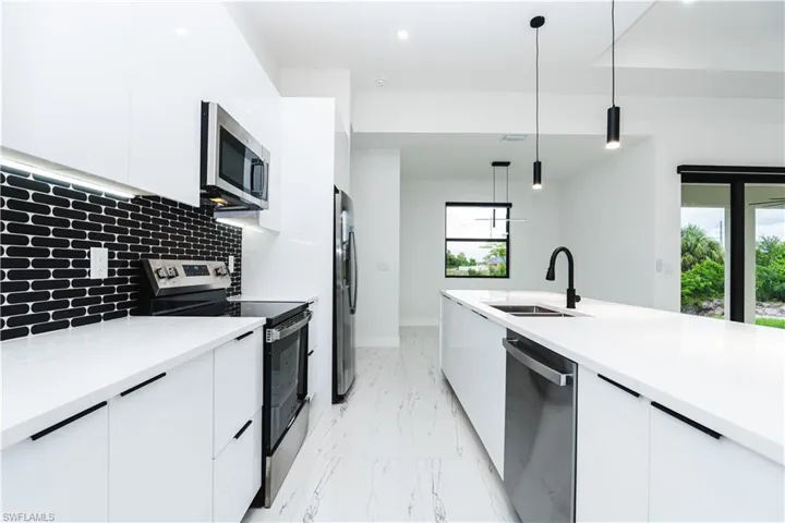 Kitchen with modern cabinets, appliances with stainless steel finishes, white cabinetry, pendant lighting, and decorative backsplash