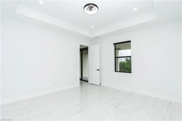 Unfurnished room featuring a raised ceiling, light marble finish floors, and recessed lighting