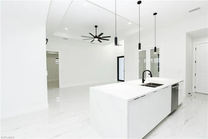 Kitchen featuring white cabinetry, hanging light fixtures, modern cabinets, a center island with sink, and light stone counters