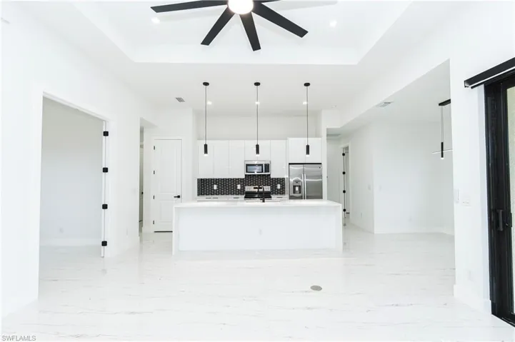 Kitchen with a tray ceiling, backsplash, a center island with sink, stainless steel appliances, and recessed lighting
