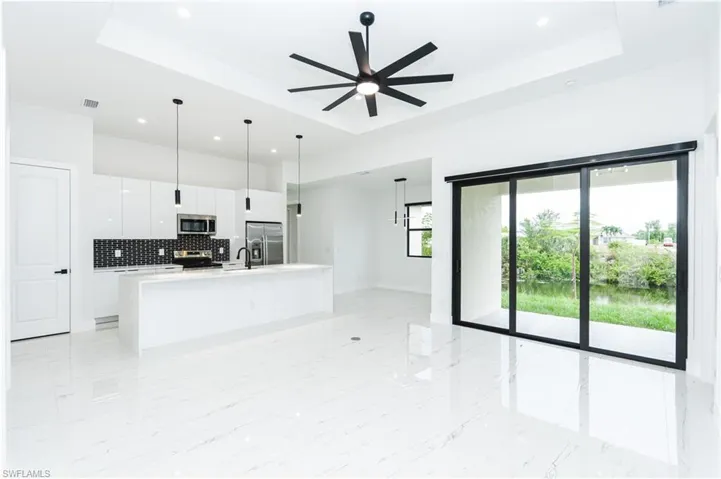 Unfurnished living room with a raised ceiling, light marble finish flooring, recessed lighting, ceiling fan, and a water view