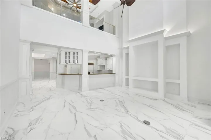 Family-room with light marble finish flooring, a ceiling fan and high ceilings.