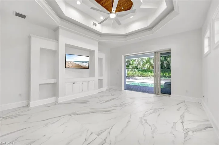 Ground floor primary bedroom featuring built in cabinets, light marble finish floors, ceiling fan, recessed lighting and sliding door to pool area.