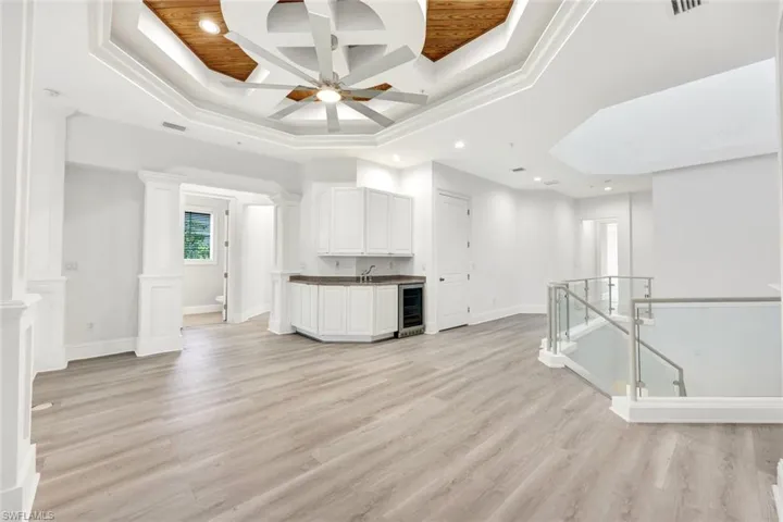 Upstairs sitting area with coffered ceiling, light wood-style flooring, beam ceiling, a tray ceiling and wet-bar.