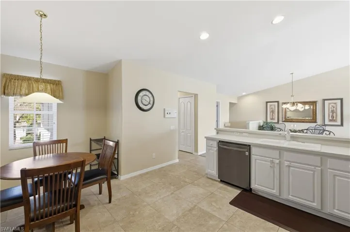 Kitchen featuring decorative light fixtures, dishwasher, light countertops, white cabinetry, and vaulted ceiling