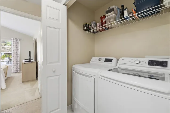 Laundry area with lofted ceiling, independent washer and dryer, light carpet, and light tile patterned floors