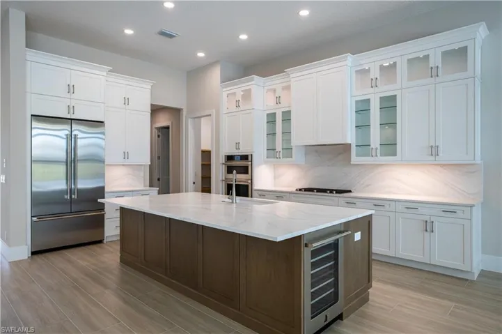 Kitchen with appliances with stainless steel finishes, wine cooler, white cabinetry, a center island with sink, and recessed lighting