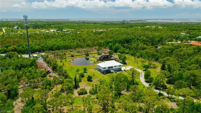 Expansive natural landscaping with mature trees, private driveway, and a large pond feature