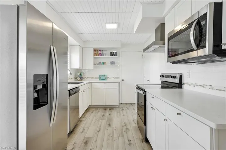 Kitchen with light hardwood / wood-style floors, tasteful backsplash, white cabinetry, wall chimney exhaust hood, and appliances with stainless steel finishes