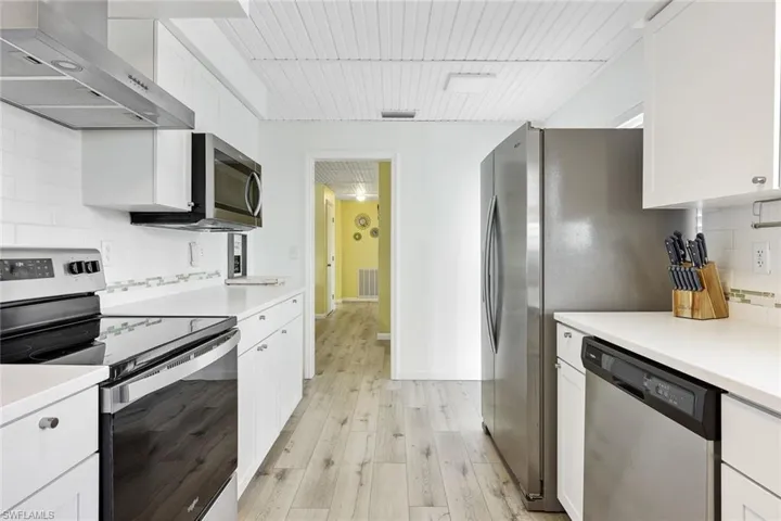 Kitchen with wall chimney range hood, light hardwood / wood-style flooring, backsplash, and appliances with stainless steel finishes