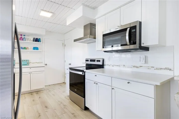 Kitchen featuring stainless steel appliances, white cabinets, wall chimney exhaust hood, and light wood-type flooring