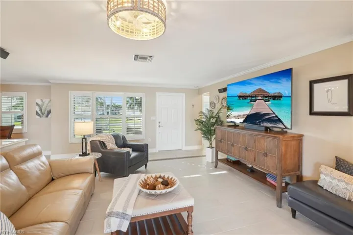 Living room with an inviting chandelier, ornamental molding, light tile patterned flooring, and plenty of natural light