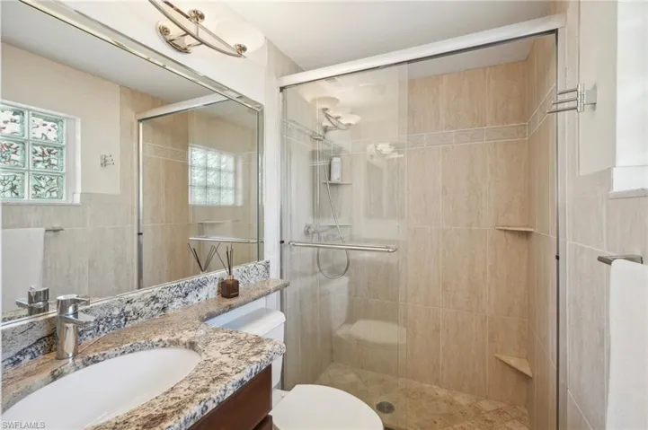 Bathroom featuring walk in shower, vanity, toilet, and tile walls