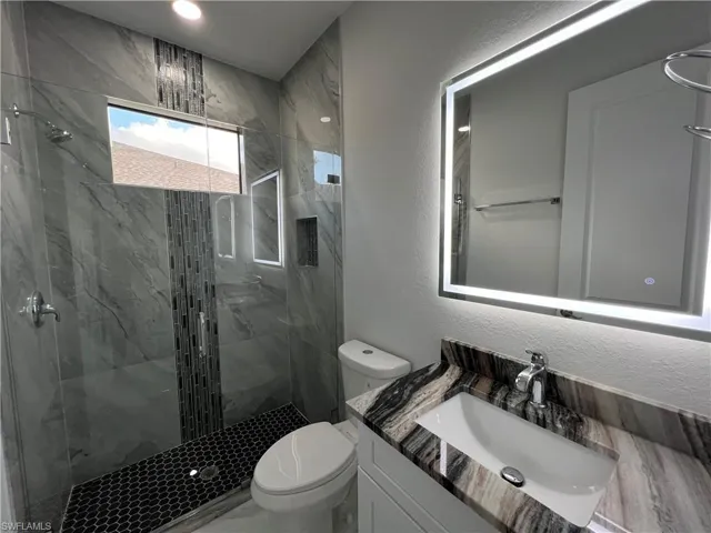 Bathroom 2 featuring a textured wall, vanity, and a marble finish shower