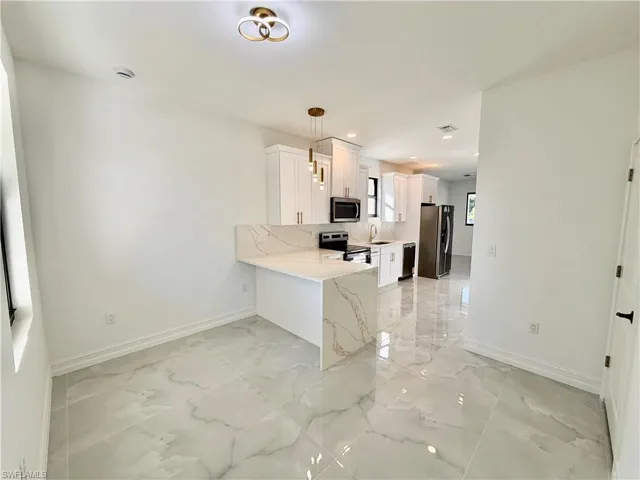 Kitchen featuring a peninsula, stainless steel appliances, decorative light fixtures, light stone counters, and white cabinetry