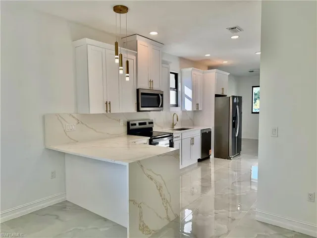 Kitchen with a peninsula, light stone countertops, stainless steel appliances, white cabinetry, and light marble finish flooring