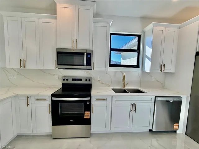 Kitchen with stainless steel appliances, backsplash, light stone counters, and white cabinetry