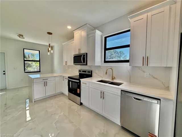 Kitchen featuring stainless steel appliances, decorative backsplash, white cabinets, and pendant lighting
