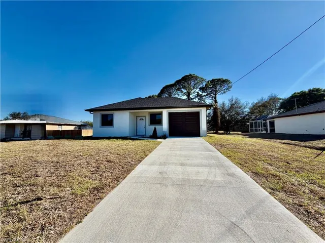 Ranch-style home featuring a front lawn, stucco siding, driveway, and a garage