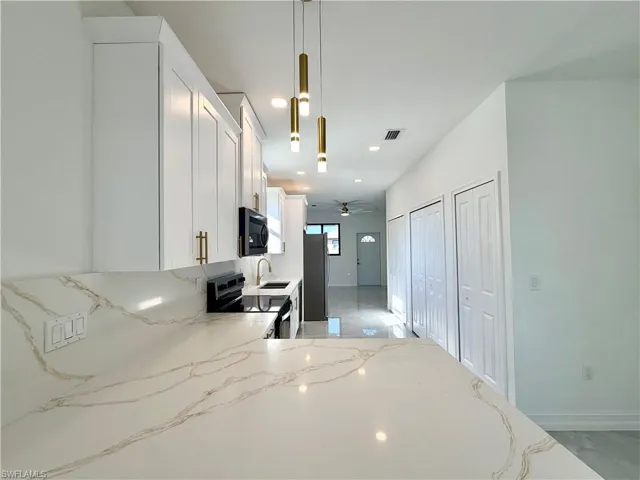 Kitchen featuring white cabinetry, range with electric stovetop, hanging light fixtures, light stone counters, and black microwave