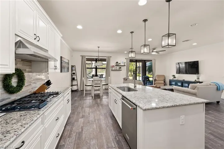 Kitchen with ornamental molding, a sink, under cabinet range hood, dark wood finished floors, and appliances with stainless steel finishes