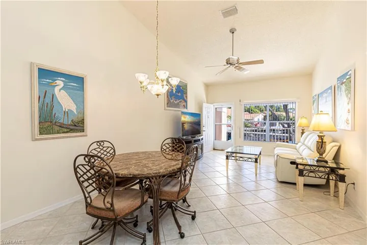 Dining area with a chandelier, ceiling fan, light tile patterned flooring & high vaulted ceiling.