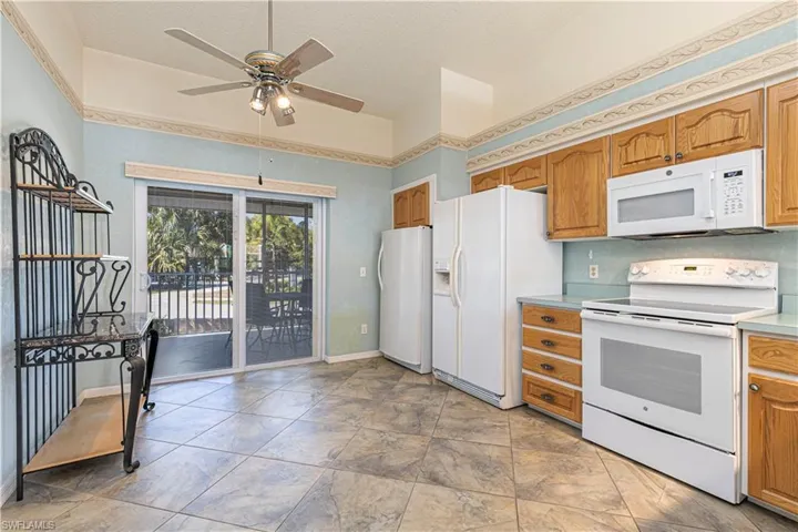 Kitchen featuring white appliances, brown cabinetry, light countertops & ceiling fan.
