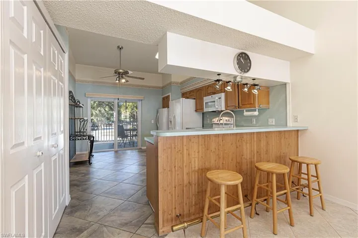 Kitchen w/ breakfast bar, light countertops, brown cabinetry & white appliances.