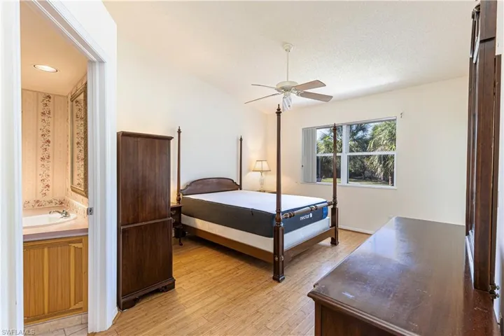 Primary bedroom with light wood-type flooring, ceiling fan & ensuite bathroom.