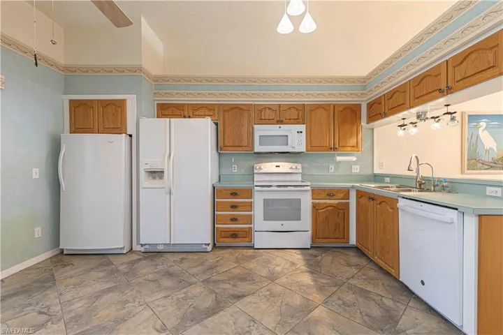 Kitchen featuring white appliances, brown cabinetry, light countertops & ceiling fan.