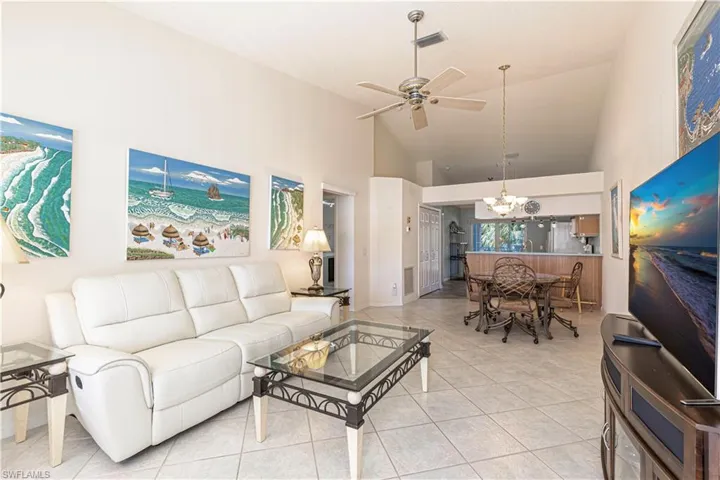 Living room w/ ceiling fan, high vaulted ceiling, tile patterned flooring & chandelier.