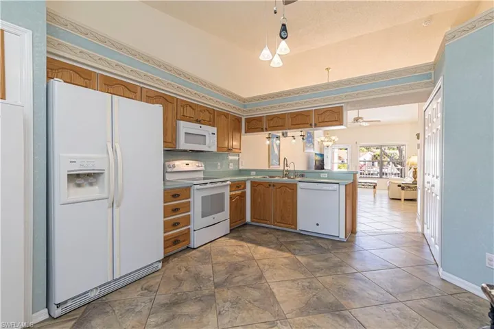 Kitchen featuring white appliances, brown cabinetry, light countertops & ceiling fan.