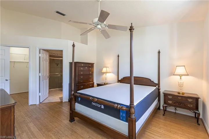 Primary bedroom featuring spacious walk-in closet, light wood-style flooring, a ceiling fan & lofted ceiling.