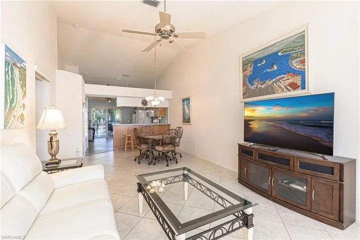 Living room w/ ceiling fan, high vaulted ceiling, tile patterned flooring & chandelier.