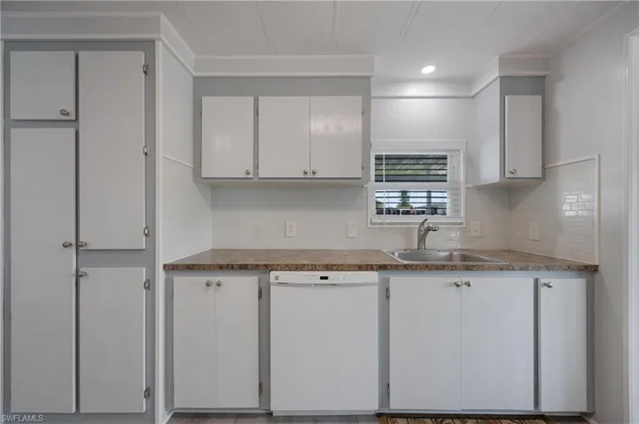 Kitchen featuring white cabinetry, crown molding, white dishwasher, and sink