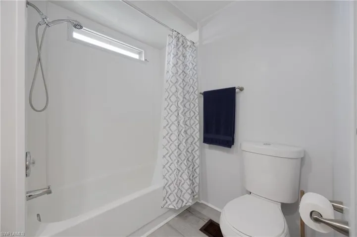 Bathroom featuring toilet, shower / bath combination with curtain, and wood-type flooring