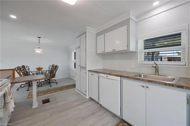 Kitchen with dishwasher, sink, decorative light fixtures, white cabinetry, and light hardwood / wood-style floors