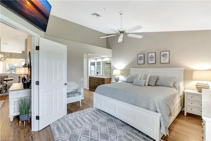 Bedroom with wood finished floors, multiple windows, ensuite bathroom, a ceiling fan, and high vaulted ceiling