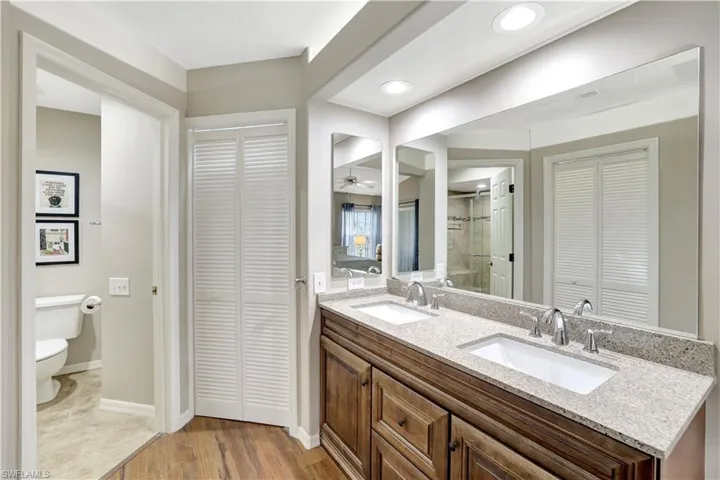 Bathroom with a closet, double vanity, a tile shower, wood finished floors, and recessed lighting